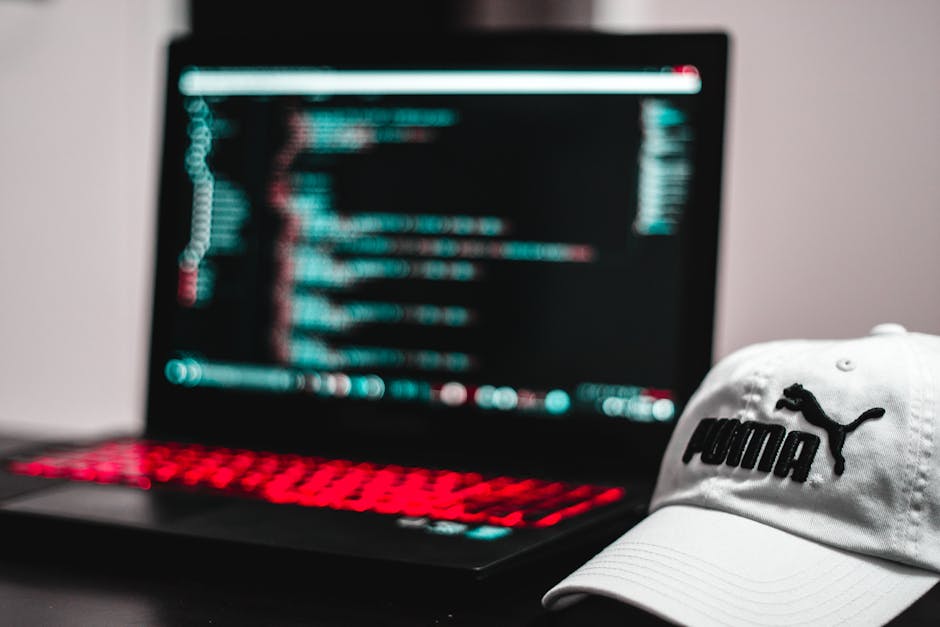 A close-up view of a laptop displaying lines of code on a dark background, positioned on a wooden desk. Next to the laptop is a ceramic mug with text that reads 'THIS COFFEE IS MAKING ME AWESOME,' whi